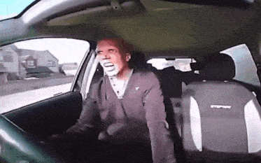 a man is sitting in a car with his mouth open .