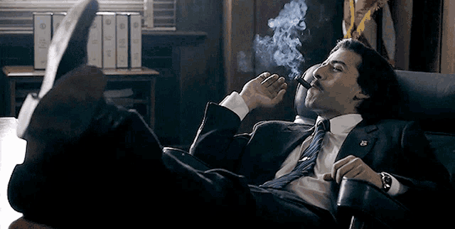 a man in a suit and tie is smoking a cigar with his feet up