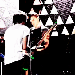 a man is playing a guitar in front of a microphone while another man looks on