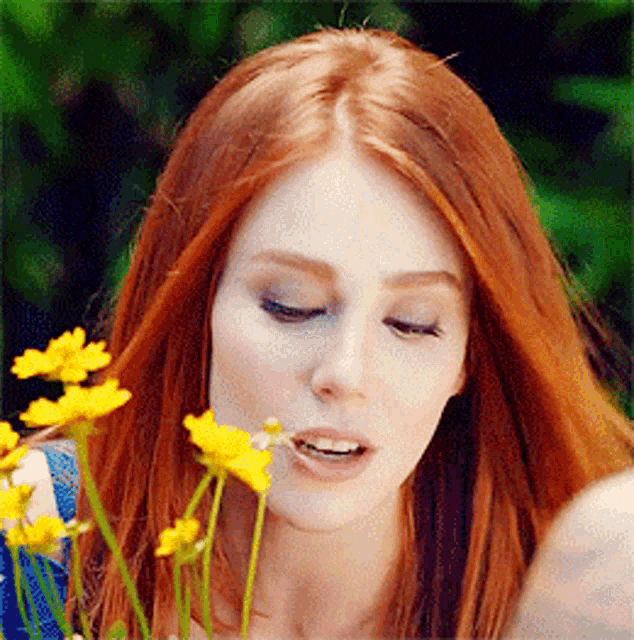 a woman with red hair is smelling a bunch of flowers