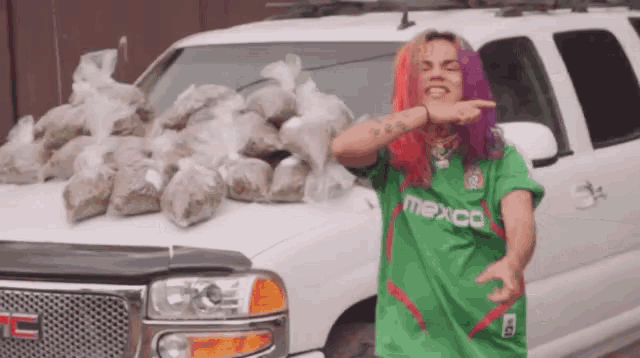 a man in a green shirt is standing in front of a white suv filled with bags of drugs .