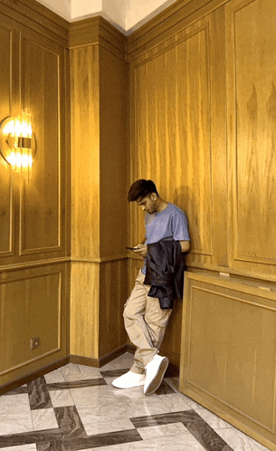 a man leaning against a wall looking at his cell phone
