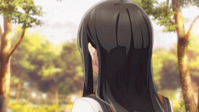 a girl with long black hair is standing in a park with trees in the background