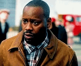 a man wearing a plaid shirt and a brown jacket has a surprised look on his face