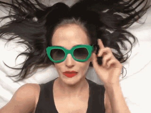 a woman wearing green sunglasses and red lips is laying on a bed