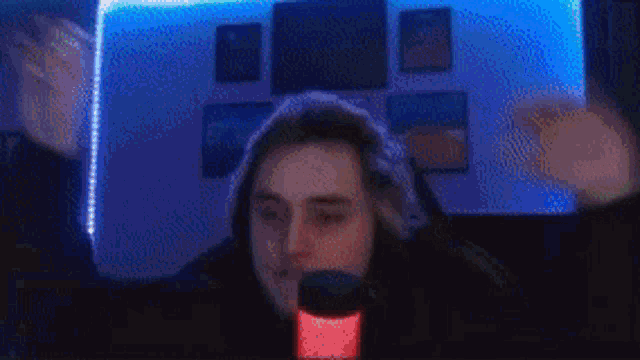 a man in a hoodie is sitting in front of a microphone with his hands in the air .