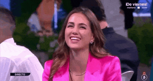 a woman in a pink jacket is laughing while sitting in a chair on a television show .