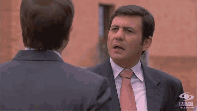 a man in a suit and tie is talking to another man in a suit and tie with caracol television in the background