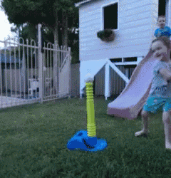 a little girl playing with a tee ball in front of a house