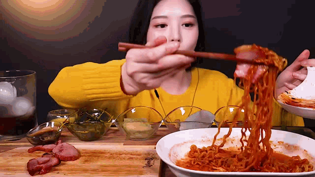 a woman in a yellow sweater is holding chopsticks over a bowl of noodles