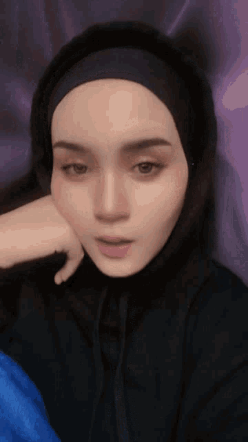 a woman wearing a hijab and a black hoodie looks at the camera