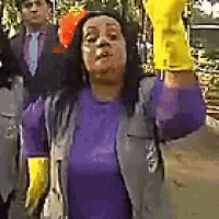 a woman wearing a purple shirt and yellow gloves is standing next to a man in a suit and tie .
