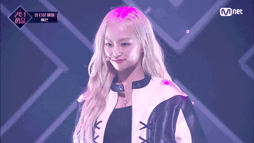 a woman with blonde hair is on a stage with a mnet logo above her