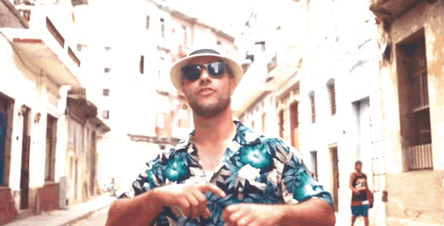 a man wearing a hat and sunglasses is standing in a street