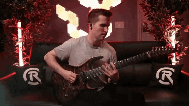 a man sits on a couch playing a guitar with a r on the pillows