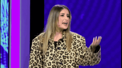 a woman wearing a leopard print jacket stands in front of a purple background