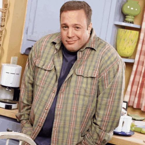 a man in a plaid shirt is standing in a kitchen with his hands in his pockets