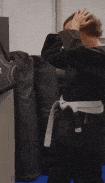 a person in a black karate uniform with a white belt is covering their face with their hands .