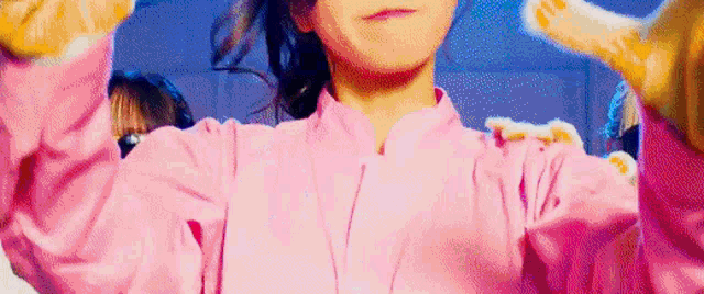 a close up of a girl in a pink shirt making a heart shape with her hands .