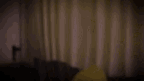 a blurry picture of a person standing in a dark room with curtains .