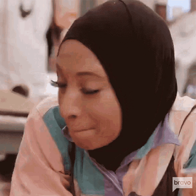 a woman wearing a hijab and a pink shirt is crying
