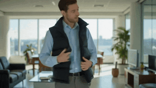 a man in a blue shirt and a black vest is standing in a living room