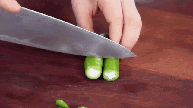 a person is cutting green peppers on a cutting board