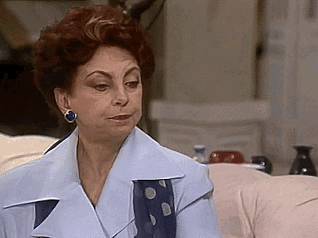 a woman with red hair is sitting on a couch wearing earrings and a blue jacket