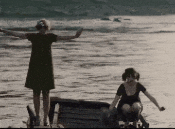 a woman in a green dress is standing in the water next to another woman in a black dress