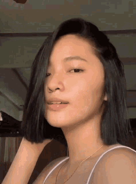 a woman with short black hair is wearing a white tank top .