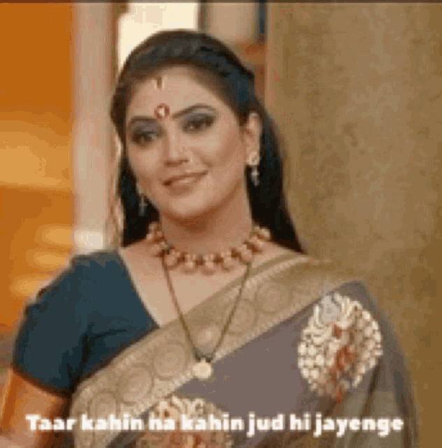 a woman is wearing a saree and a necklace and smiling .