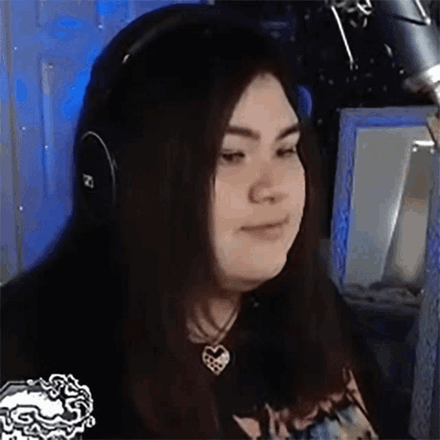 a woman wearing headphones and a heart necklace is sitting in front of a computer screen .