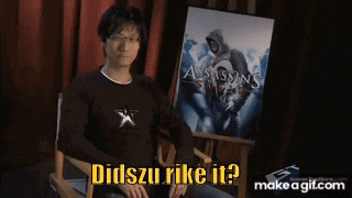 a man is sitting in front of a poster for assassin 's creed