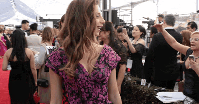 a woman in a purple floral dress stands in a crowd of people