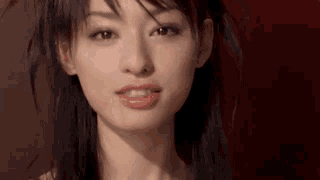 a close up of a woman 's face with a red background and her hair blowing in the wind .
