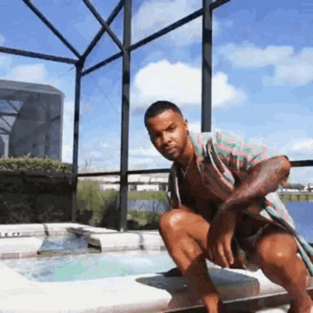a man is kneeling on the edge of a pool .