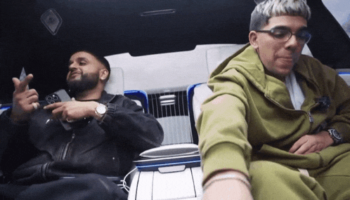 two men are sitting in a car one wearing glasses and the other wearing a watch