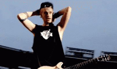 a man in a black tank top is holding a guitar while standing on a stage .