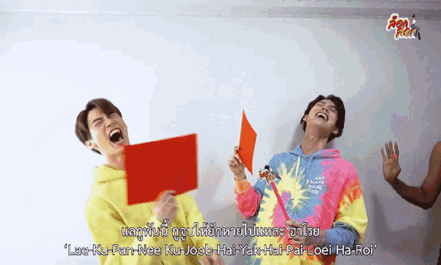 a man in a tie dye hoodie holds a red piece of paper in his mouth