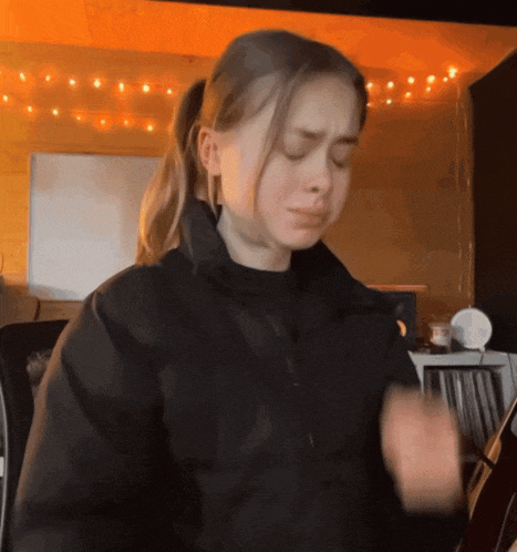 a girl in a black jacket is making a face with her eyes closed