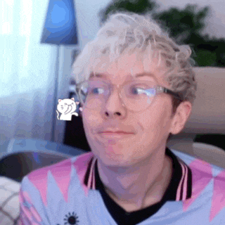 a man wearing glasses and a pink shirt is sitting in a chair and smiling .