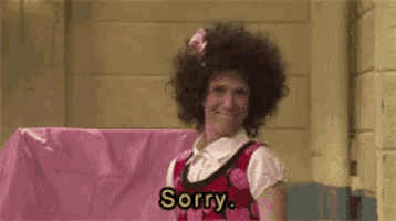 a woman with curly hair is standing in front of a pink wall and says sorry .