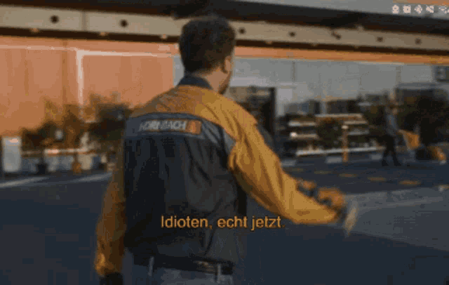 a man wearing a hornach jacket walks in front of a building