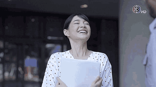 a woman is smiling and holding a piece of paper in front of a tv screen that says 3 hd
