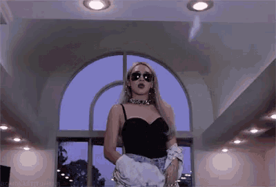 a woman wearing sunglasses and a black top is standing in front of a large window .
