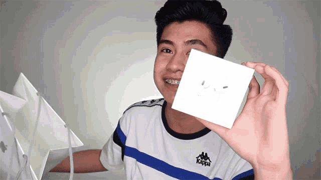a young man wearing a kappa shirt holds up a small square