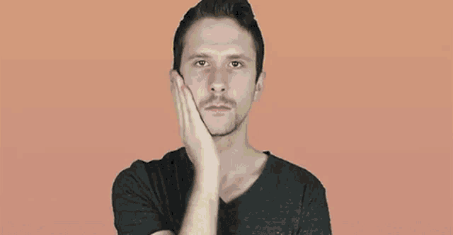 a man with a mustache is holding his hand to his face and looking at the camera .