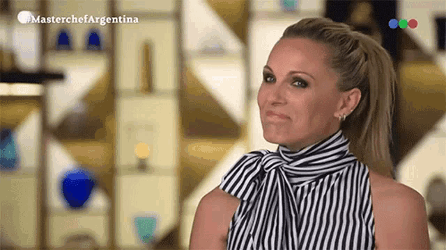 a woman wearing a black and white striped shirt is standing in front of a wall with a masterchef argentina logo on it
