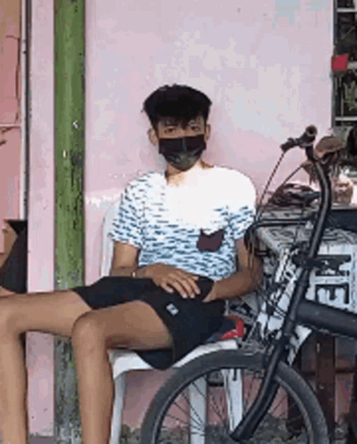 a young man wearing a mask sits on a chair next to a bike