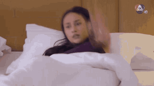 a woman is laying on a bed with a tv channel in the background ..